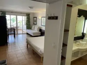 Vue intérieure d'un studio Bardadine, type rénové en version vert Tropical. Vue partielle de la salle de bain et de la chambre